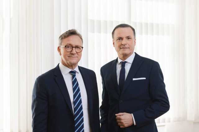 Executive Directors Ettl and Müller standing in front of a white curtain